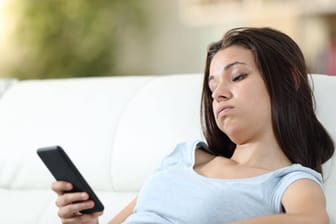 Eine Frau schaut genervt auf ihr Handy (Symbolbild): Vorsicht vor Spam-Anrufen.