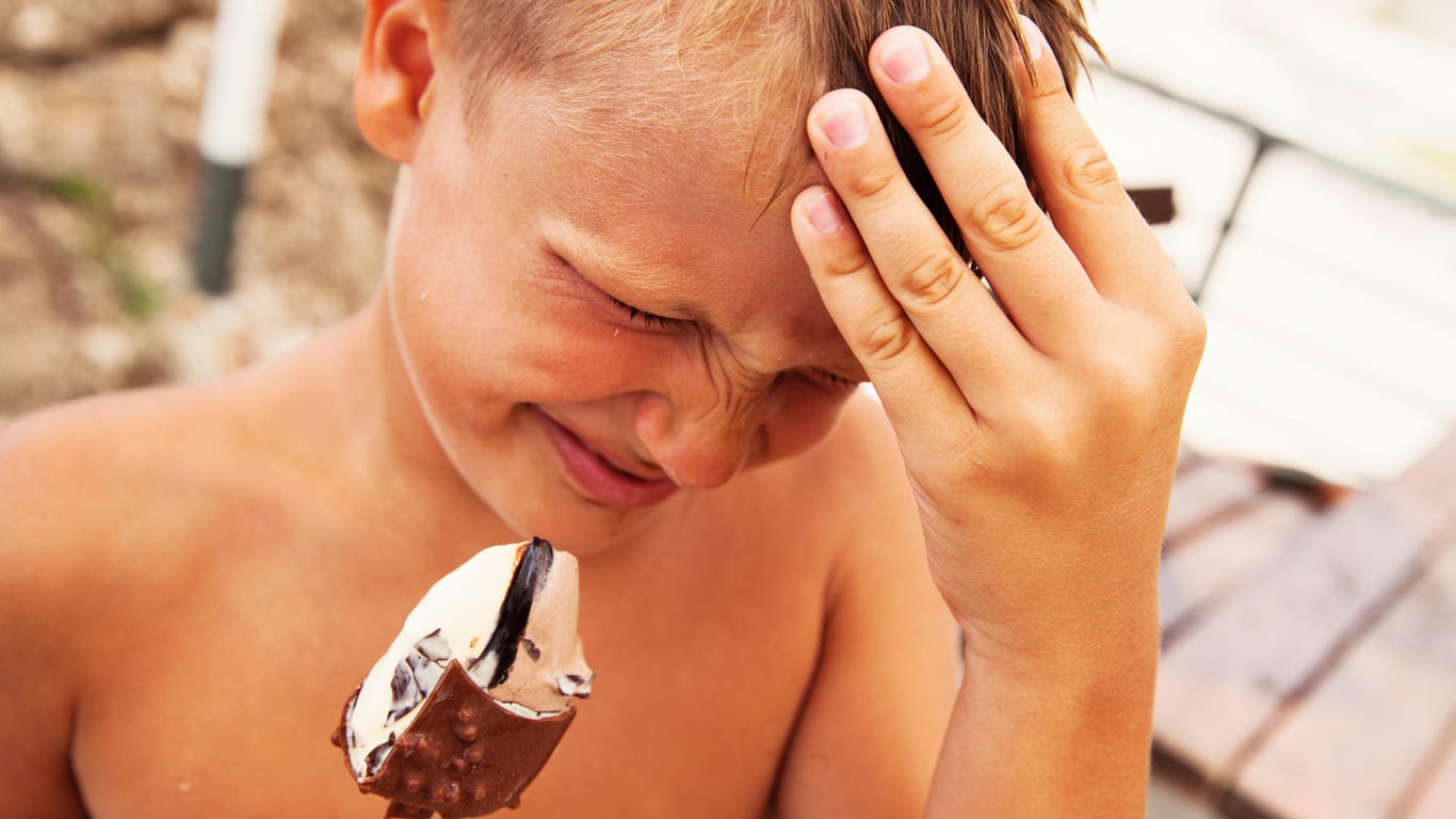 Ein Junge isst Eis und hält sich schmerzverzerrt den Kopf.