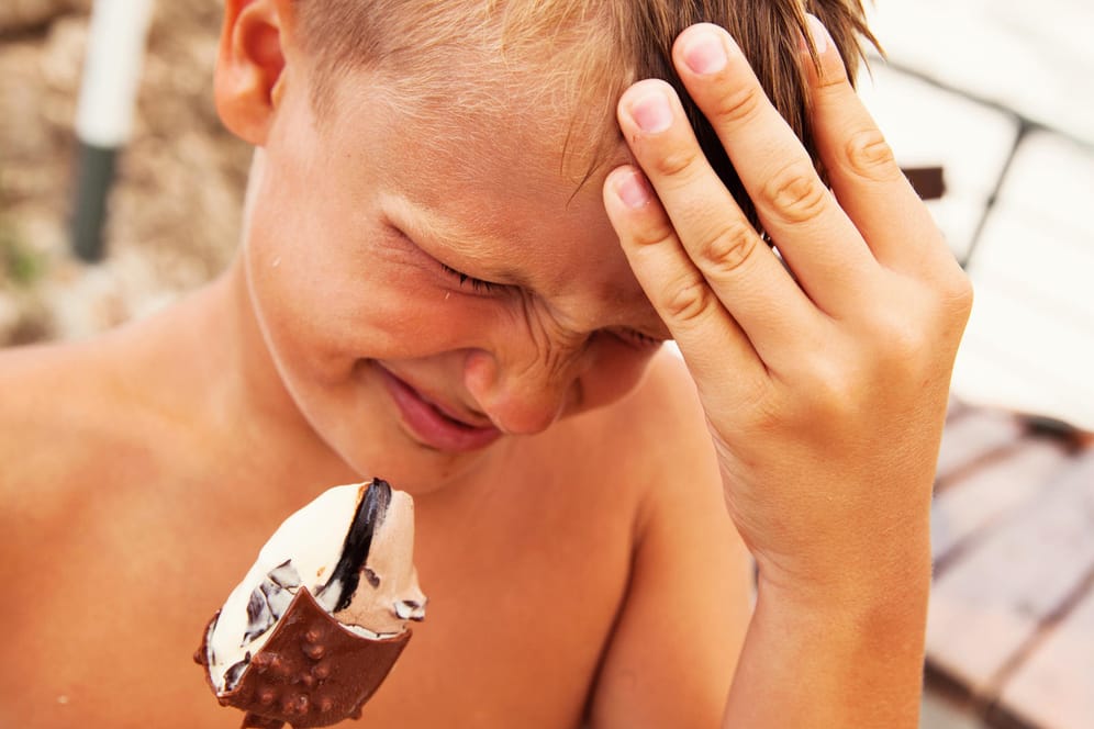 Ein Junge isst Eis und hält sich schmerzverzerrt den Kopf.