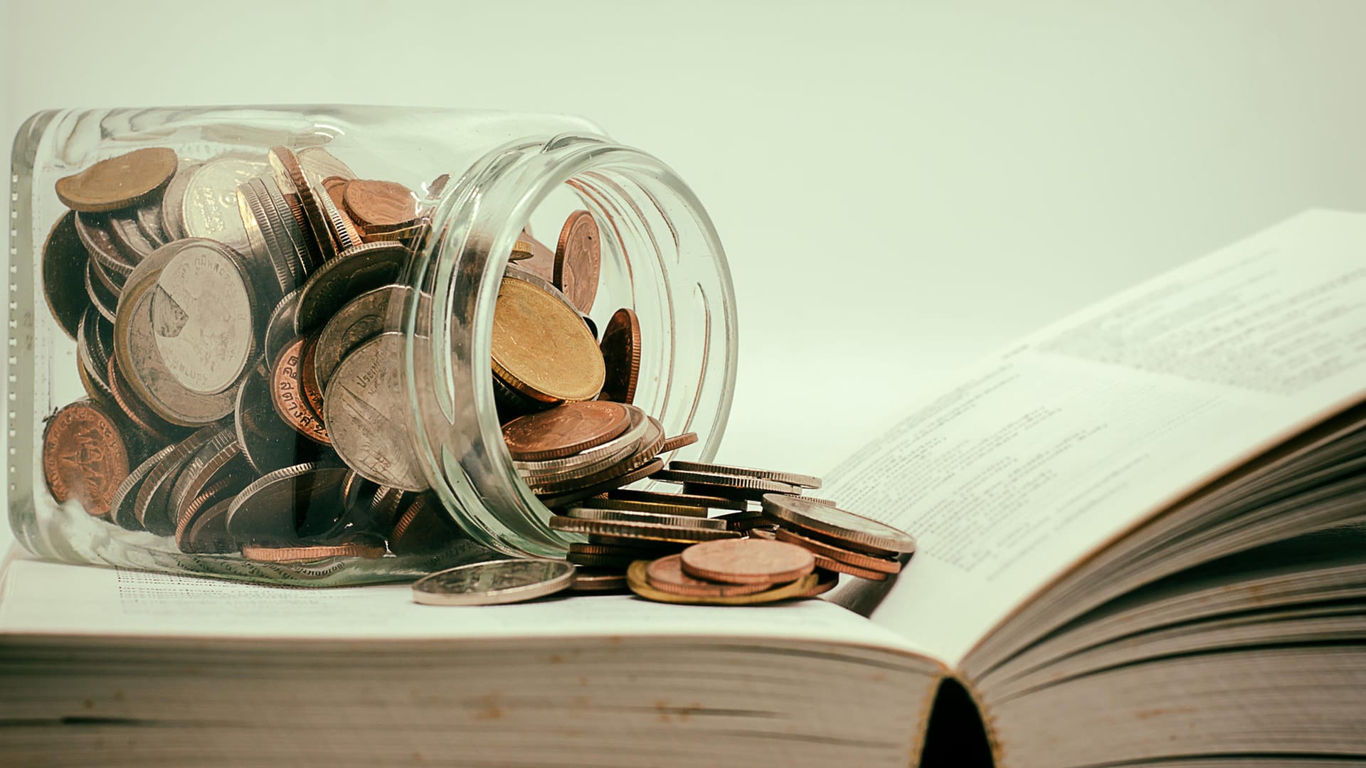 Glas mit Münzen auf einem Buch: Neben dem Auslands-BAföG können Studierende auch Zuschläge beantragen.