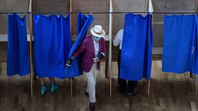 Ein Mann verlässt in einem Wahllokal eine Wahlkabine.