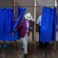 Ein Mann verlässt in einem Wahllokal eine Wahlkabine.