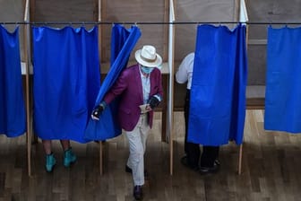 Ein Mann verlässt in einem Wahllokal eine Wahlkabine.