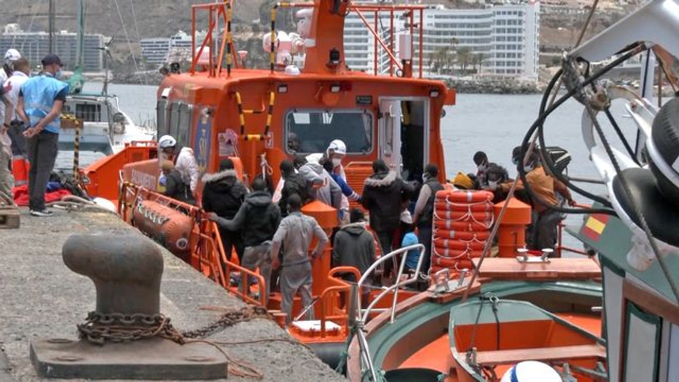Mitarbeiter in Schutzkleidung der Salvamento Maritimo helfen im Hafen von Arguineguin Migranten an Land.