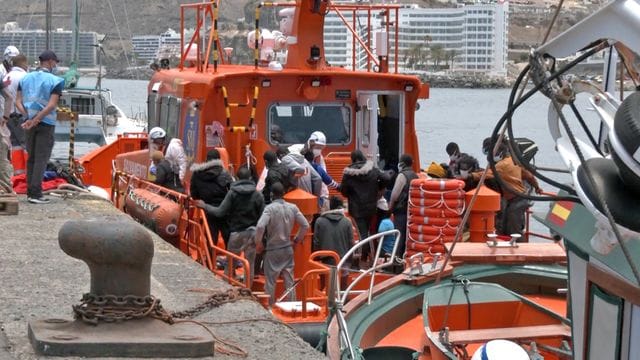 Mitarbeiter in Schutzkleidung der Salvamento Maritimo helfen im Hafen von Arguineguin Migranten an Land.