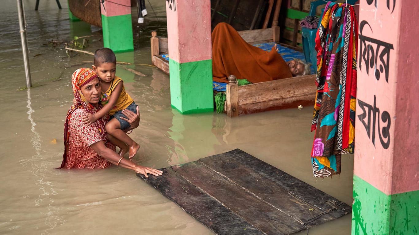 Bangladesch: Eine Frau trägt ihr Kind durchs Hochwasser. Naturkatastrophen wie Überschwemmungen und Wirbelstürme, aber auch Dürren kommen durch den Klimawandel häufiger vor und bringen Hunderttausende Kinder in Gefahr.