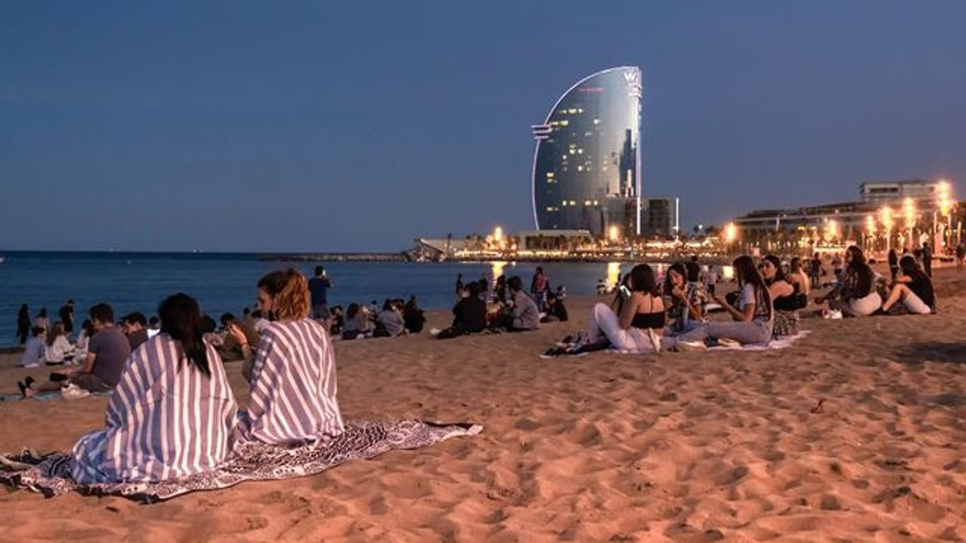 Junge Menschen sitzen in Barcelona, Katalonien, mit Abstand voneinander am Strand.