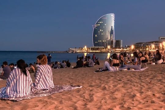 Junge Menschen sitzen in Barcelona, Katalonien, mit Abstand voneinander am Strand.