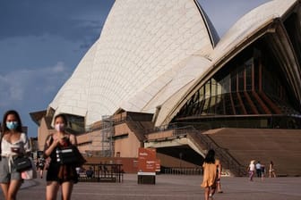 Passanten mit Mund-Nasen-Bedeckung gehen am berühmten Opernhaus in Sydney vorbei.