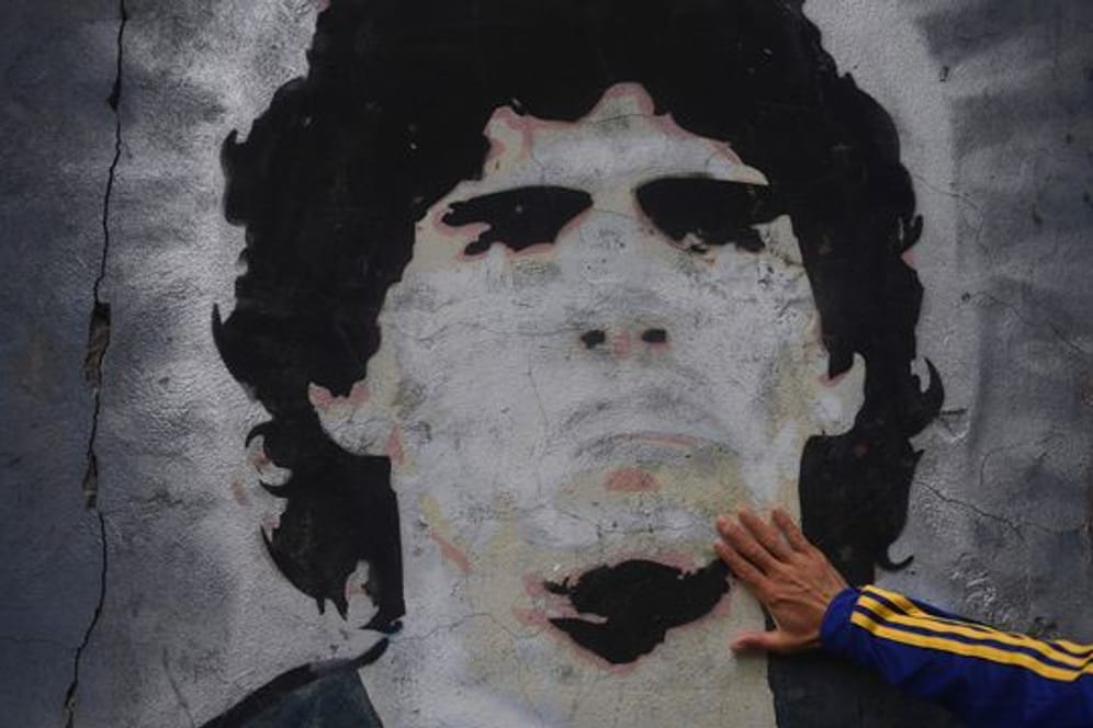 Ein Fan trauert vor einem Wandgemälde mit der Abbildung des ehemaligen Fußballstars Maradona.