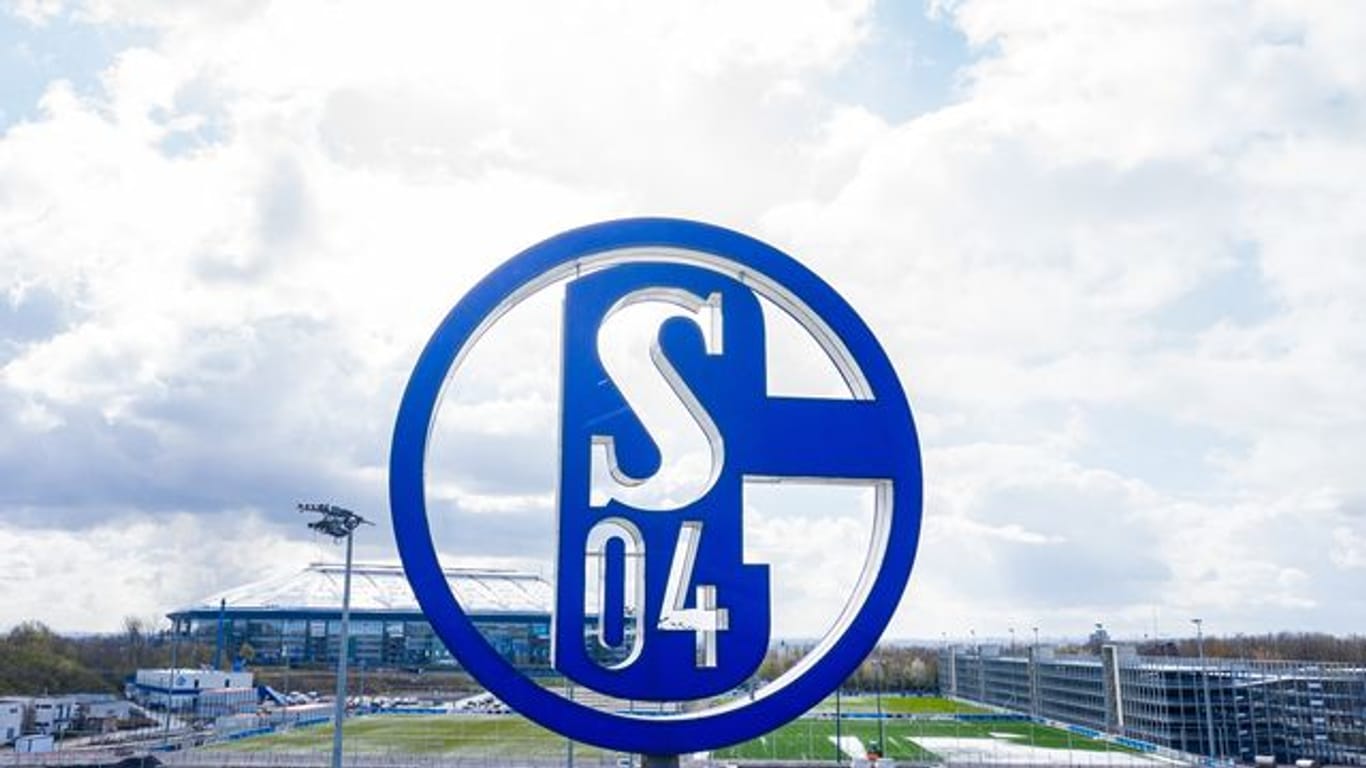 Im Vordergrund dreht sich das Logo des FC Schalke auf der Geschäftsstelle; im Hintergrund steht die Veltins Arena.