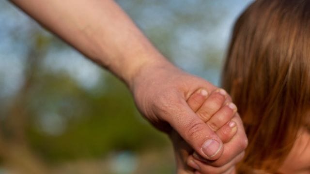 Ein junger Vater hält am Strand eines Sees die Hand seines kleinen Sohnes.