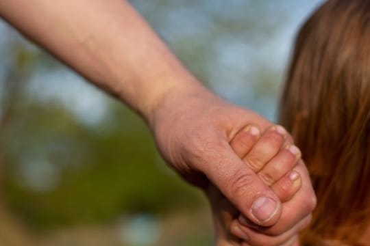 Ein junger Vater hält am Strand eines Sees die Hand seines kleinen Sohnes.