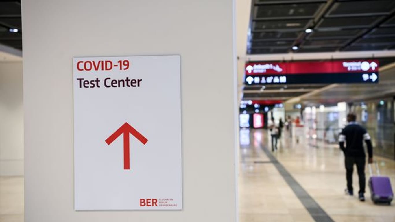 Ein Reisender geht im Flughafen Berlin-Brandenburg (BER) mit einem Koffer nahe eines Hinweisschildes mit der Aufschrift "Covid-19 Test Center".