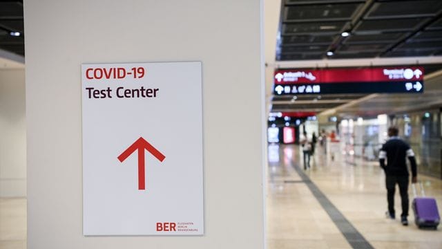 Ein Reisender geht im Flughafen Berlin-Brandenburg (BER) mit einem Koffer nahe eines Hinweisschildes mit der Aufschrift "Covid-19 Test Center". Ein Reisender geht im Flughafen Berlin-Brandenburg (BER) mit einem Koffer nahe eines Hinweisschildes mit der Aufschrift "Covid-19 Test Center".