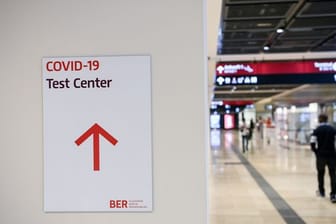 Ein Reisender geht im Flughafen Berlin-Brandenburg (BER) mit einem Koffer nahe eines Hinweisschildes mit der Aufschrift "Covid-19 Test Center".