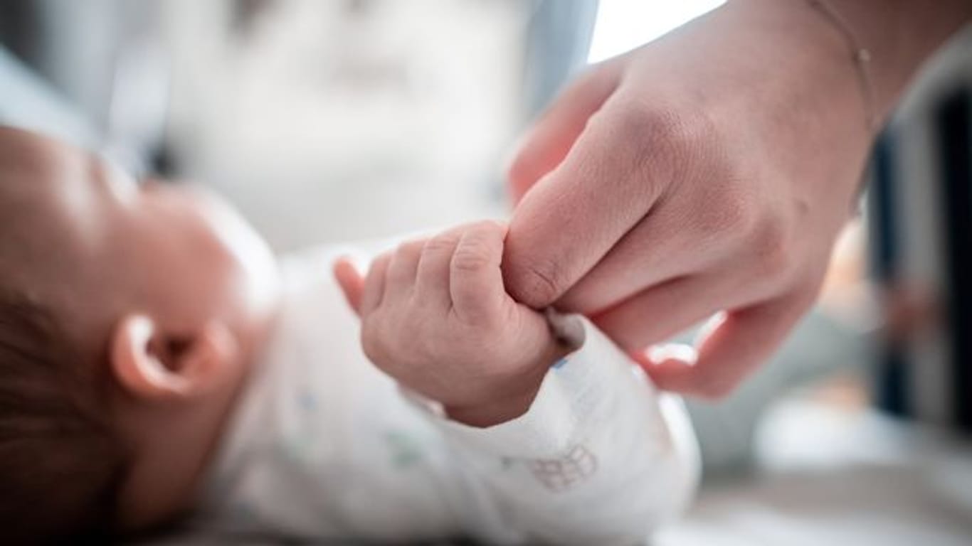 Ein Baby klammert sich an einen Finger seiner Mutter.