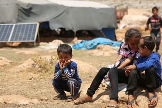 Geflüchtete Kinder sitzen in einem Flüchtlingslager nordwestlich von Aleppo auf einem Stein.
