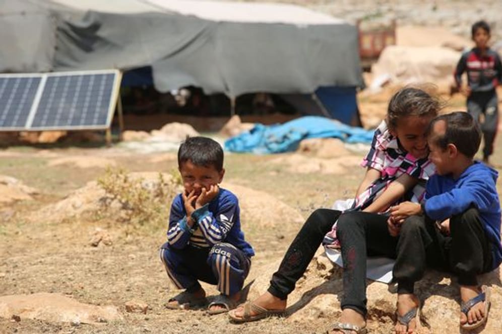 Geflüchtete Kinder sitzen in einem Flüchtlingslager nordwestlich von Aleppo auf einem Stein.