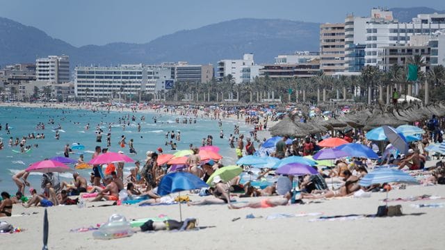 Touristen genießen die Sonne am Strand von Arenal.