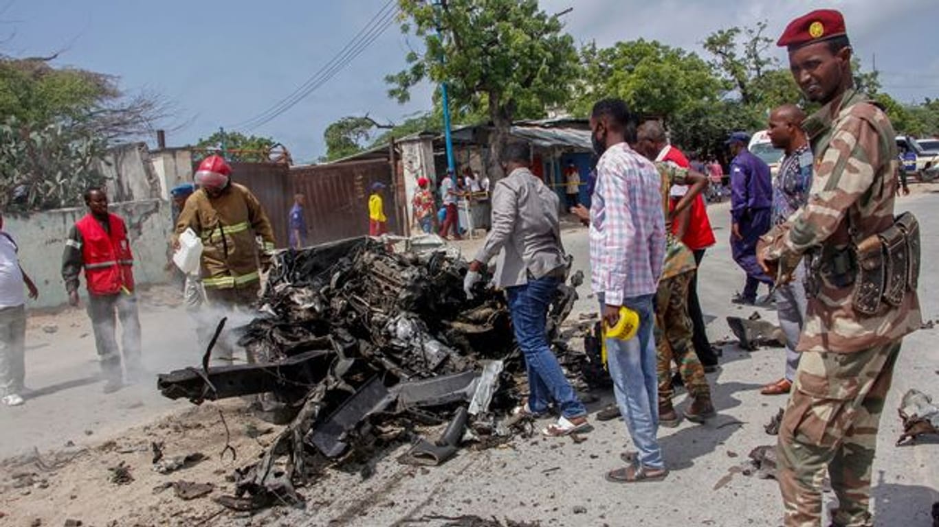 Sicherheitskräfte und Zivilisten stehen in der Nähe eines Autowracks nach dem ersten Anschlag im somalischen Mogadischu.