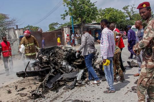 Sicherheitskräfte und Zivilisten stehen in der Nähe eines Autowracks nach dem ersten Anschlag im somalischen Mogadischu.