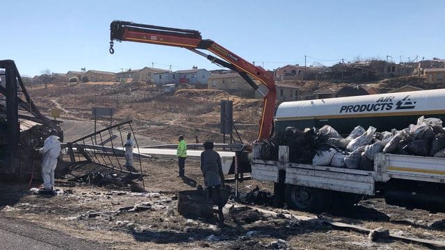 Arbeiter stehen in der Provinz Kwa-Zulu Natal neben den verkohlten Trümmern an einer Mautstelle, an der zuvor gewalttätige Demonstranten, die gegen die Haftstrafe von Ex-Präsident Zuma protestierten, mehrere Autos und Lastwagen in Brand gesteckt hatten.