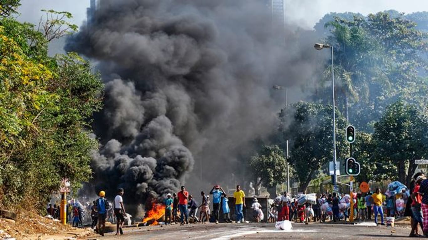 Plünderer stehen in Durban vor einem Einkaufszentrum neben einer brennenden Barrikade.