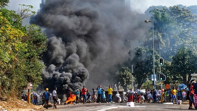 Plünderer stehen in Durban vor einem Einkaufszentrum neben einer brennenden Barrikade. Plünderer stehen in Durban vor einem Einkaufszentrum neben einer brennenden Barrikade.