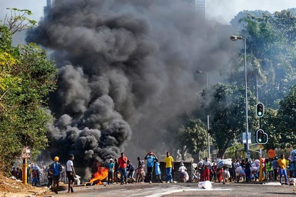 Plünderer stehen in Durban vor einem Einkaufszentrum neben einer brennenden Barrikade.