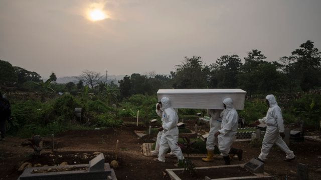 Menschen in Schutzkleidung tragen einen Sarg auf einem indonesischen Friedhof. Menschen in Schutzkleidung tragen einen Sarg auf einem indonesischen Friedhof.