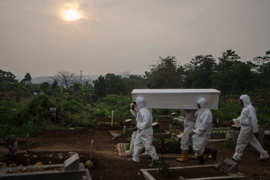 Menschen in Schutzkleidung tragen einen Sarg auf einem indonesischen Friedhof.