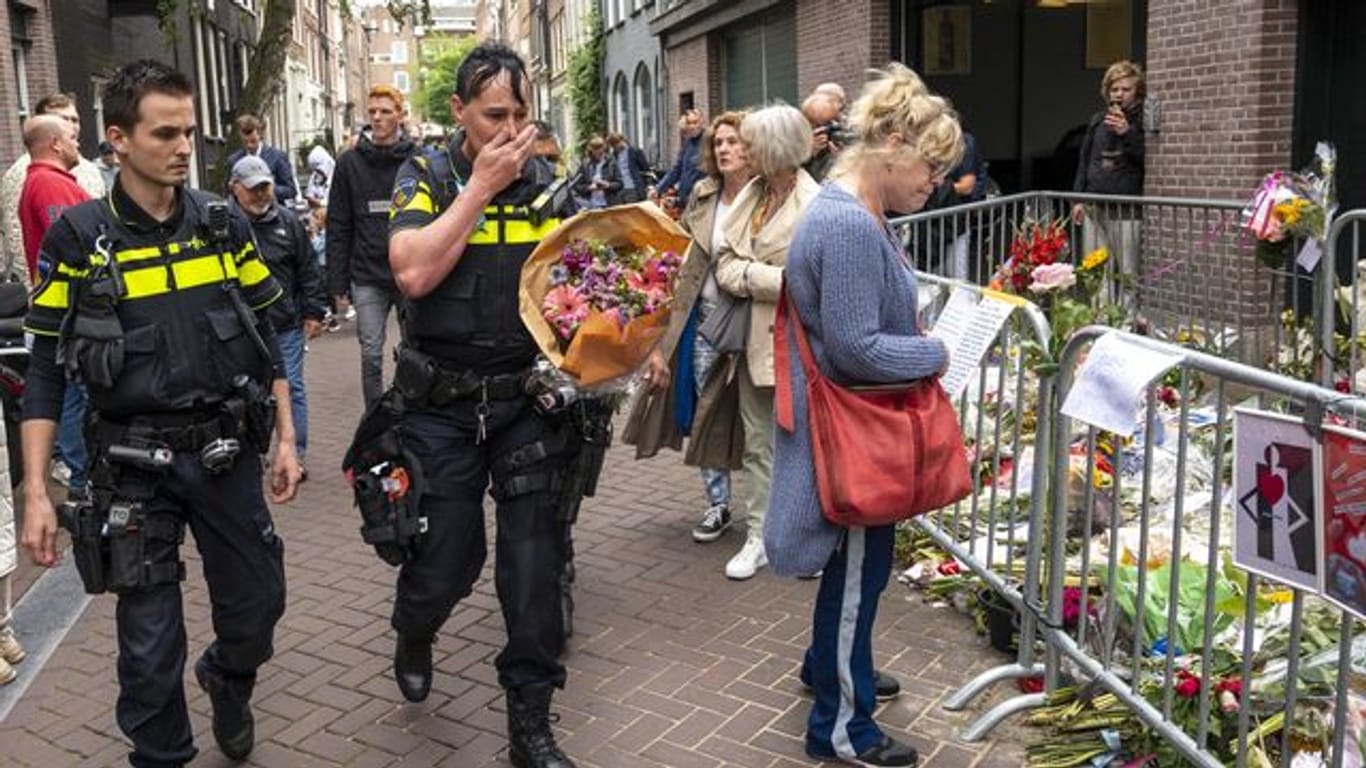 Polizisten bringen einen Blumenstrauß zu dem Blumenmeer für den Reporter Peter R.