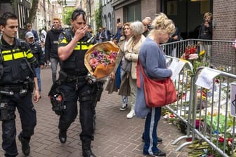 Polizisten bringen einen Blumenstrauß zu dem Blumenmeer für den Reporter Peter R.