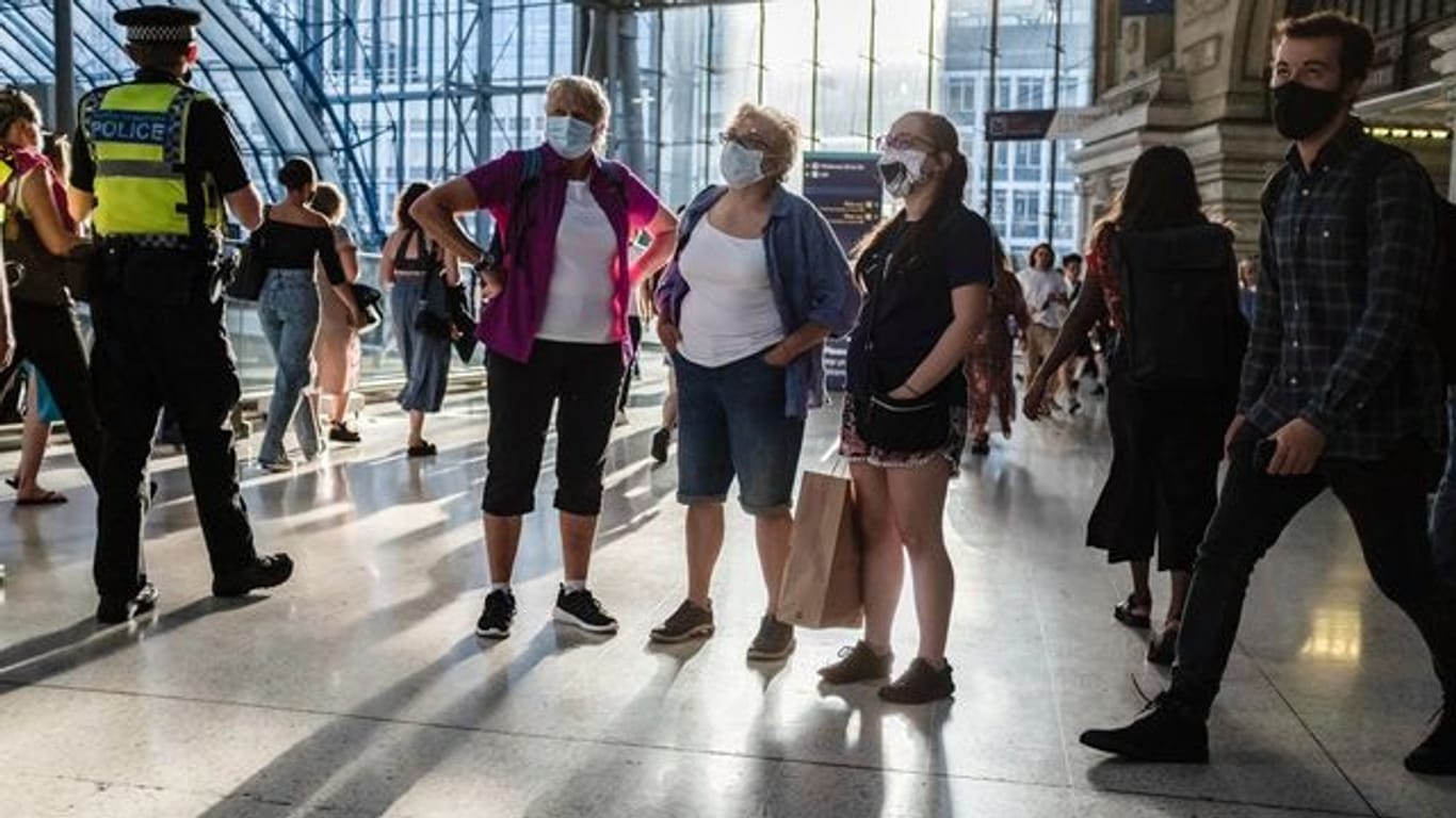 Menschen mit Mund-Nasen-Schutz stehen in einer U-Bahn Station in London.