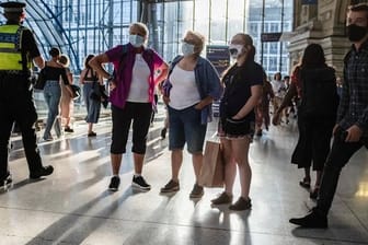 Menschen mit Mund-Nasen-Schutz stehen in einer U-Bahn Station in London.