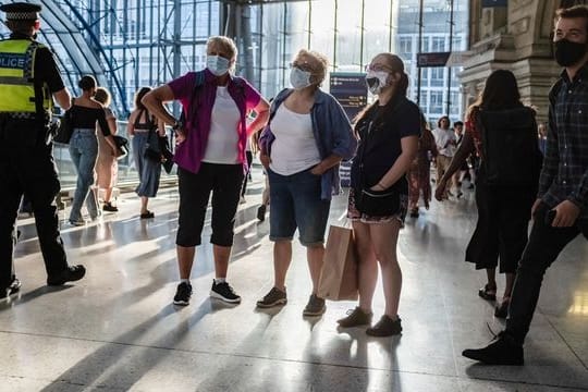 Menschen mit Mund-Nasen-Schutz stehen in einer U-Bahn Station in London.