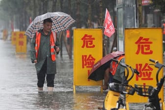 Mitarbeiter stellen Warnschilder auf mit der Aufschrift "Gefahr!" in einem überschwemmten Gebiet im Kreis Wuzhi in der zentralchinesischen Provinz Henan.