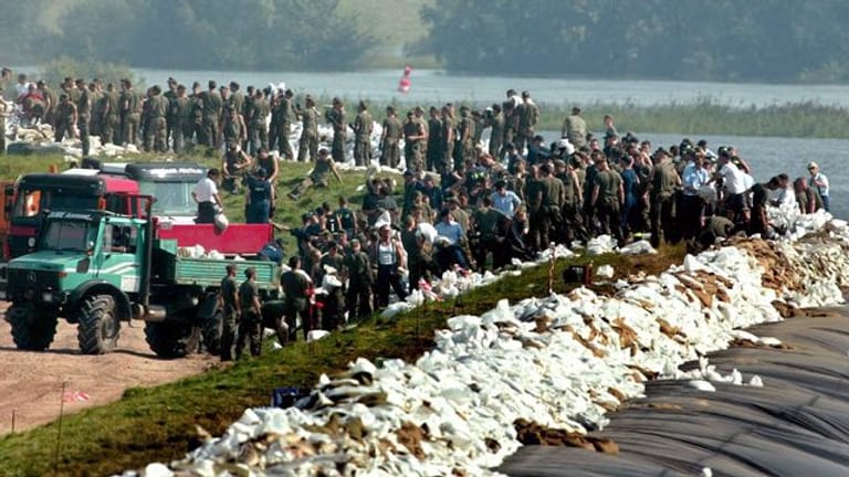 Soldaten der Bundeswehr und freiwillige Helfer sichern 2002 in der Nähe der Elbbrücke im schleswig-holsteinischen Lauenburg einen mit Folie abgedeckten Deich mit Sandsäcken.