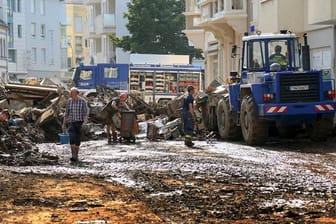 Mitarbeiter des Technischen Hilfswerks (THW) helfen bei Aufräumarbeiten nach der Unwetterkatastrophe in einer verschlammten Straße.