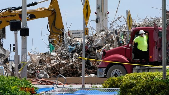 Ein Arbeiter wartet darauf, seinen Lastwagen mit Schutt aus den Trümmern des Champlain Towers South-Gebäudes zu beladen. Ein Arbeiter wartet darauf, seinen Lastwagen mit Schutt aus den Trümmern des Champlain Towers South-Gebäudes zu beladen.