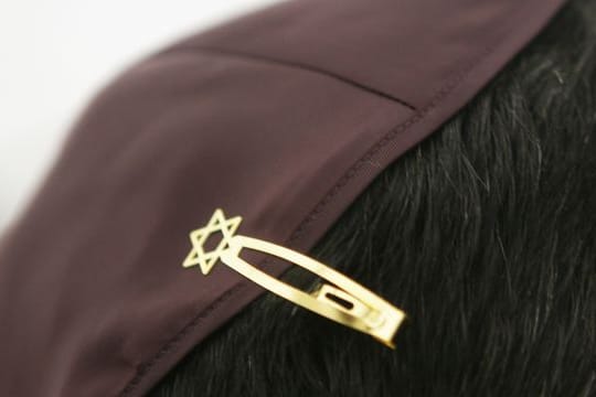 Ein Jude hat sich bei den Feierlichkeiten einer Grundsteinlegung für eine Synagoge seine Kopfbedeckung (Kippa) mit einer Davidstern-Klammer am Haar befestigt.