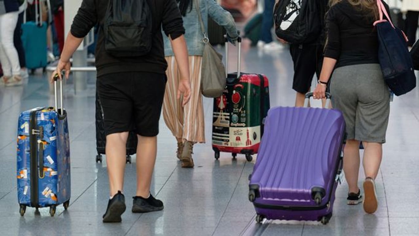 Reisende gehen im Flughafen Düsseldorf mit Koffern durch die Abflughalle.