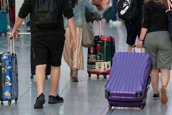 Reisende gehen im Flughafen Düsseldorf mit Koffern durch die Abflughalle.