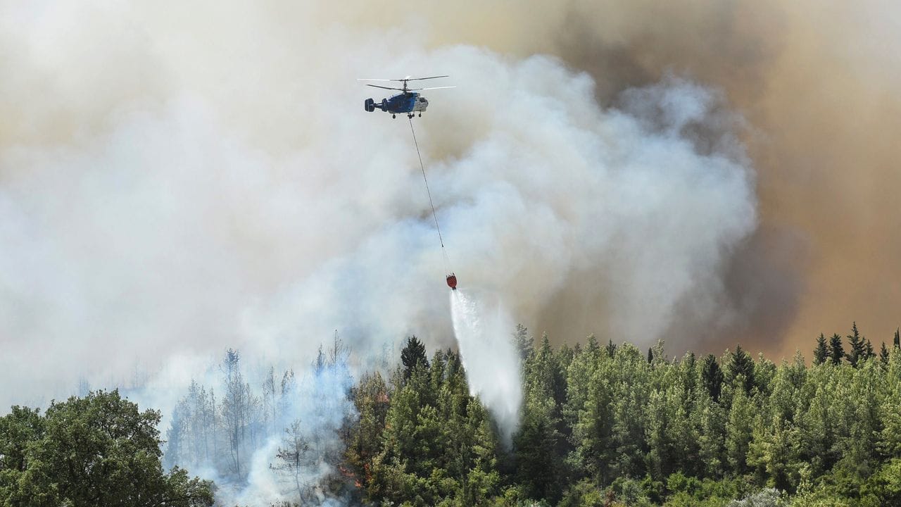 Ein Hubschrauber wirft Löschwasser über einem Waldbrände ab.