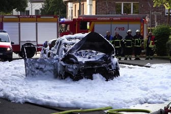 Auto-Explosion in Hürth: Das ausgebrannte Wrack des Fahrzeugs ist von Löschschaum bedeckt.