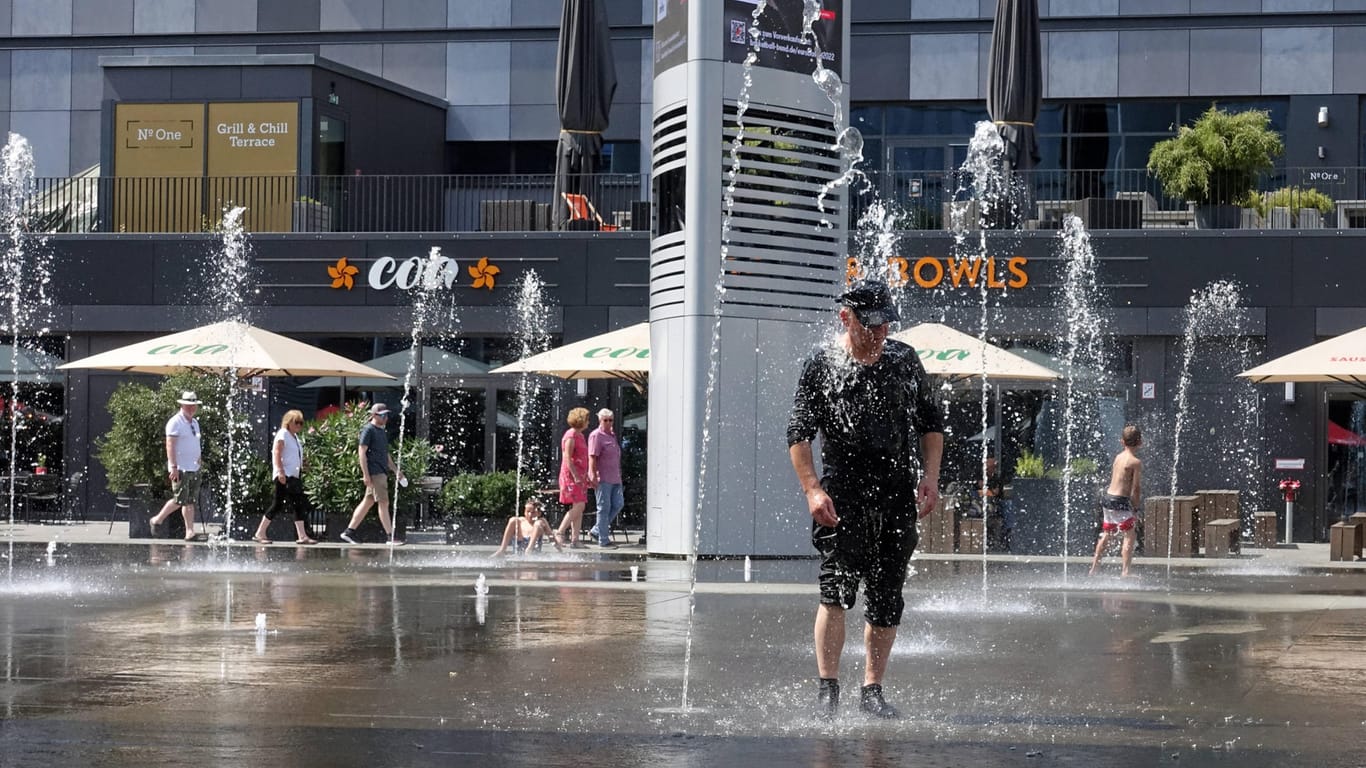 Mann steht bei sommerlichen Temperaturen unter einer Wasserfontäne: Großstädte wie Berlin müssen sich nach Einschätzung von Experten auf die Folgen des Klimawandels einstellen.