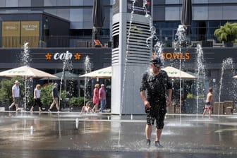 Mann steht bei sommerlichen Temperaturen unter einer Wasserfontäne: Großstädte wie Berlin müssen sich nach Einschätzung von Experten auf die Folgen des Klimawandels einstellen.