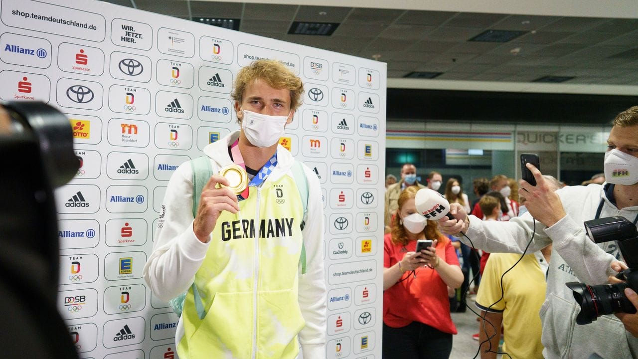 Zverev zeigt nach seiner Ankunft aus Tokio auf dem Frankfurter Flughafen seine Medaille.