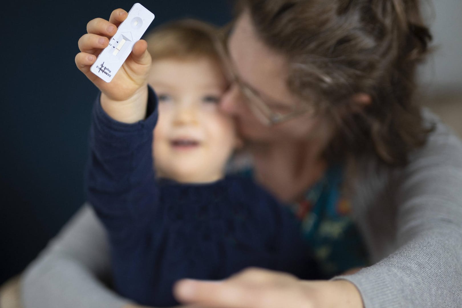 Ein Kind sitzt auf dem Schoß seiner Mutter und hält einen Corona-Test in der Hand (Symbolbild): Das Robert Koch-Institut empfiehlt flächendeckende Corona-Schnelltests in Kindertagesstätten.